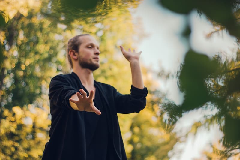 Un jeune homme épanouie dans un espace naturel, qui prend soin de son ancrage et se reconnecte à la terre, à la nature et à lui-même en faisant des mouvement.