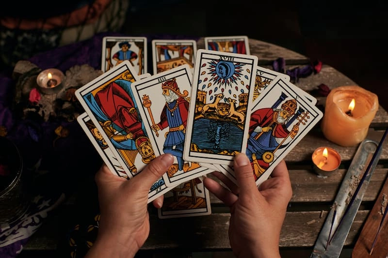 Cartes du jeu de tarot tenu en mains au dessus d'une table avec des bougies