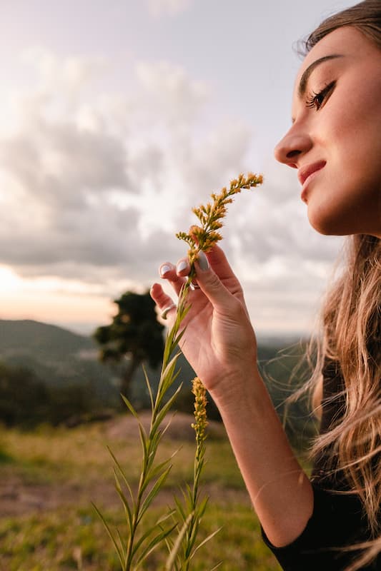 Une femme dans un champs sent l'odeur d'un brin d'herbe en souriant