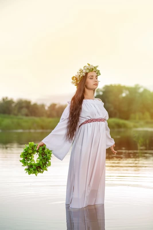 Femme sorcière néo-païenne dans l'eau en robe blanche avec une couronne de fleurs