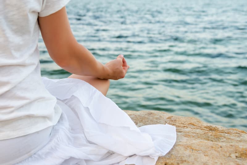 Une femme en robe blanche fait une méditation au bord de l'eau pour purifier son esprit