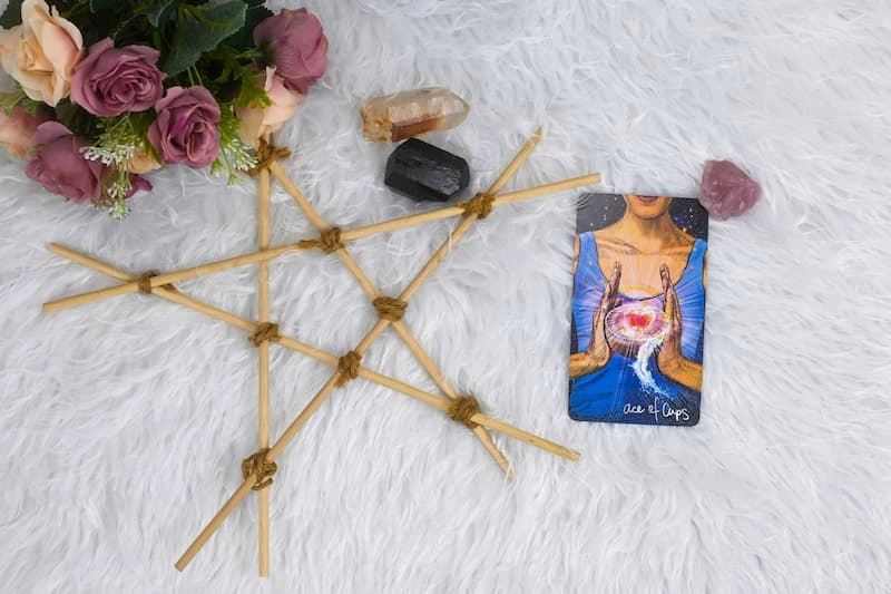 Une carte de jeu de tarot divinatoire à côté d'un pentagramme fait de branches de bois, d'un bouquet de roses et de pierres