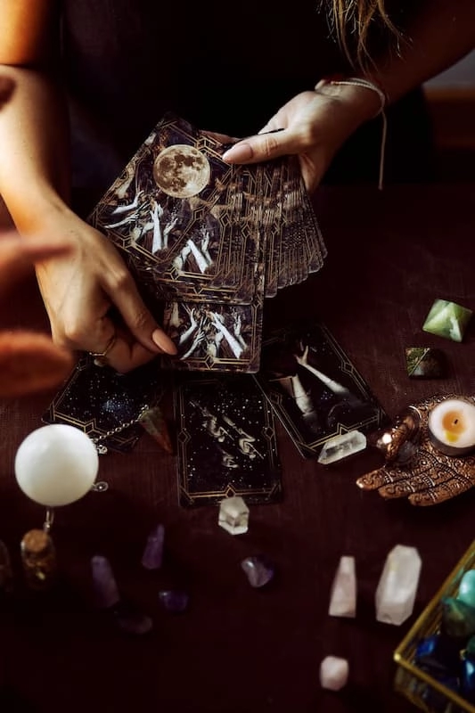 Une femme tire une carte dans un jeu de tarot au dessus d'une table avec des bougies et des pierres