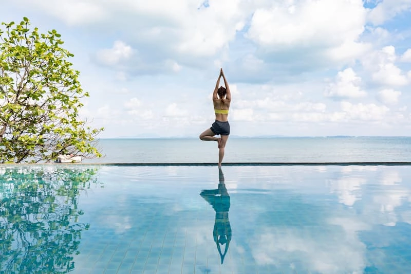 Femme qui fait du yoga en position du lotus sur l'eau dans un paysage idillique avec l'océan