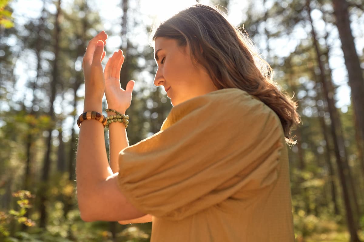 Une femme épanouie dans une forêt ensoleillée, qui prend soin de son ancrage et se reconnecte à la terre, à la nature et à elle-même.